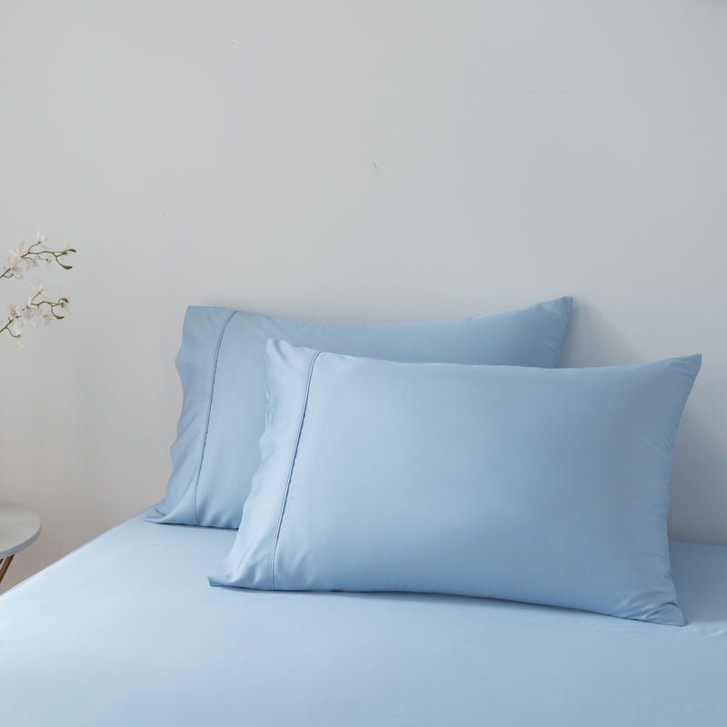 Two light blue bamboo pillows on a bed against a plain wall.