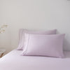 Pair of light purple bamboo pillows on a bed against a plain wall.