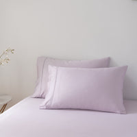 Pair of light purple bamboo pillows on a bed against a plain wall.