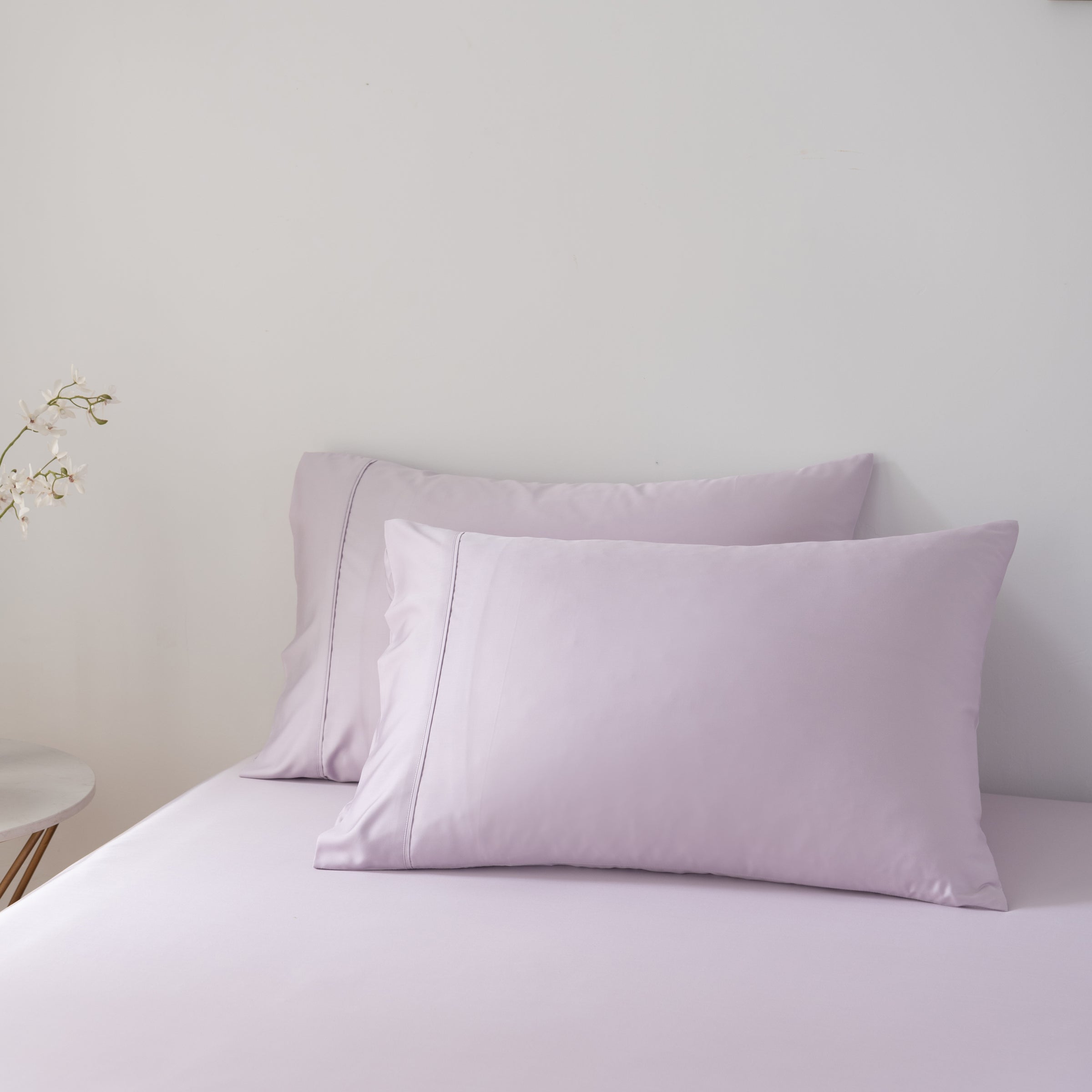 Pair of light purple bamboo pillows on a bed against a plain wall.