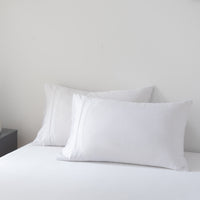 White bamboo pillows on a bed against a plain wall